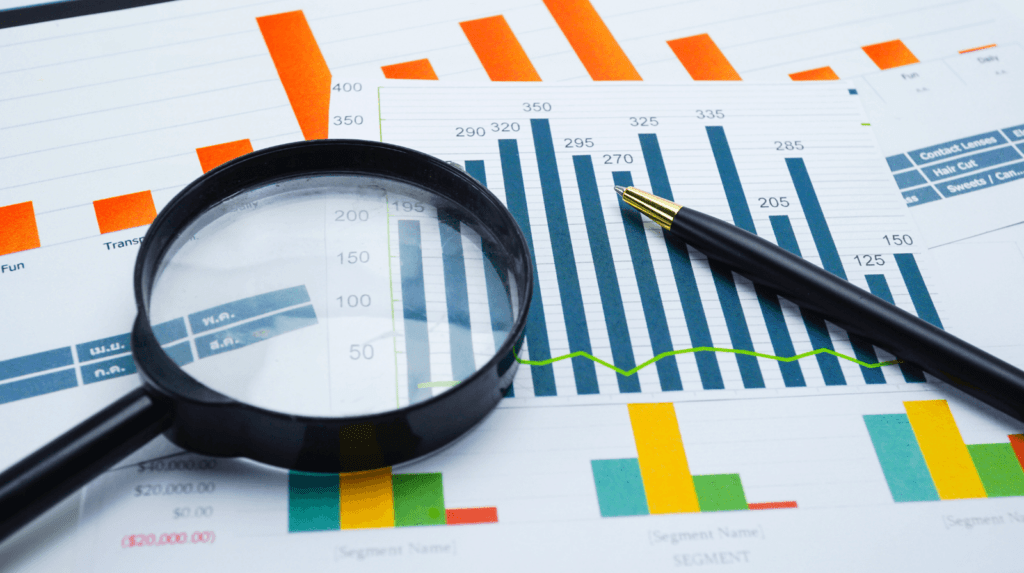 Magnifying glass and pen over a printed bar and line chart — inspecting financial data
