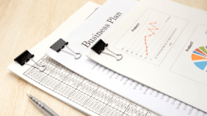 Stack of business documents and financial charts clipped together, showing graphs and data sheets, with a pen nearby — representing business review and due diligence