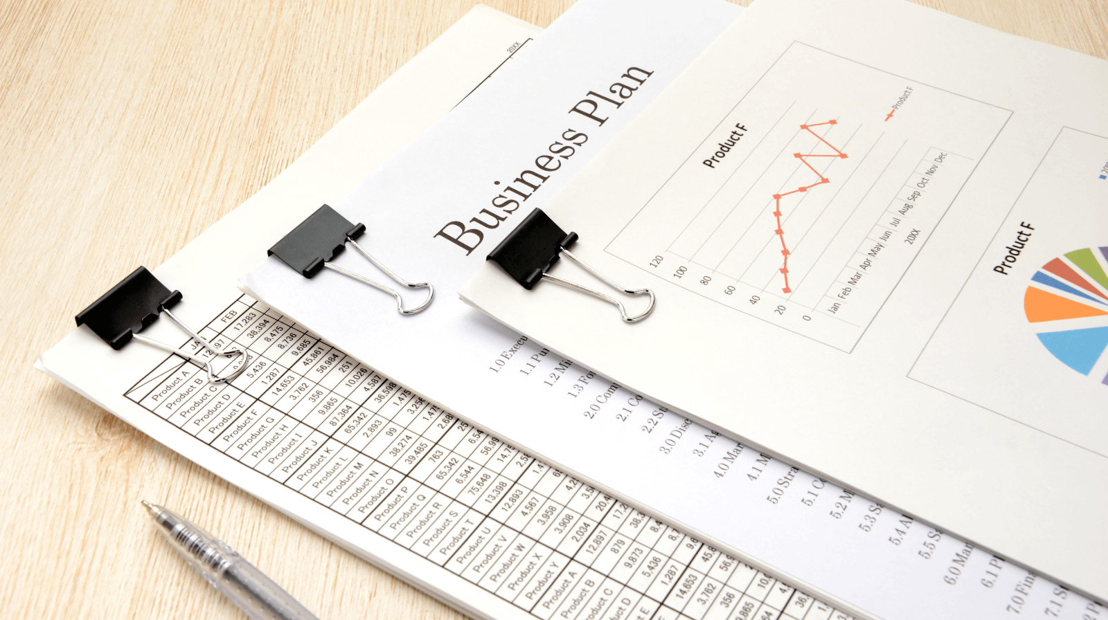 Stack of business documents and financial charts clipped together, showing graphs and data sheets, with a pen nearby — representing business review and due diligence