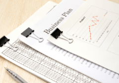 Stack of business documents and financial charts clipped together, showing graphs and data sheets, with a pen nearby — representing business review and due diligence